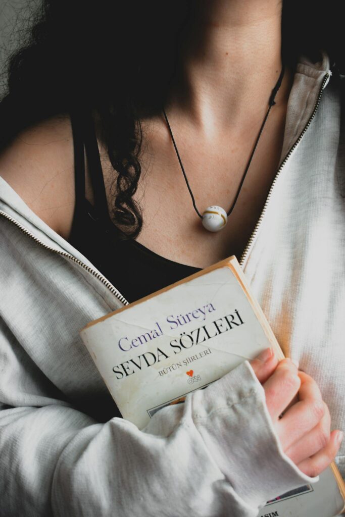 Close-up of a woman holding a Cemal Süreya poetry book with a necklace visible.
